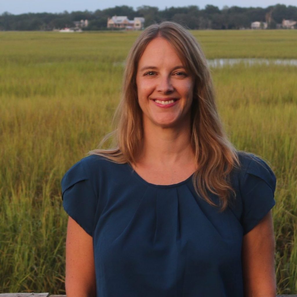 Portrait of Julie smiling in a navy blue blouse in front of a marsh.